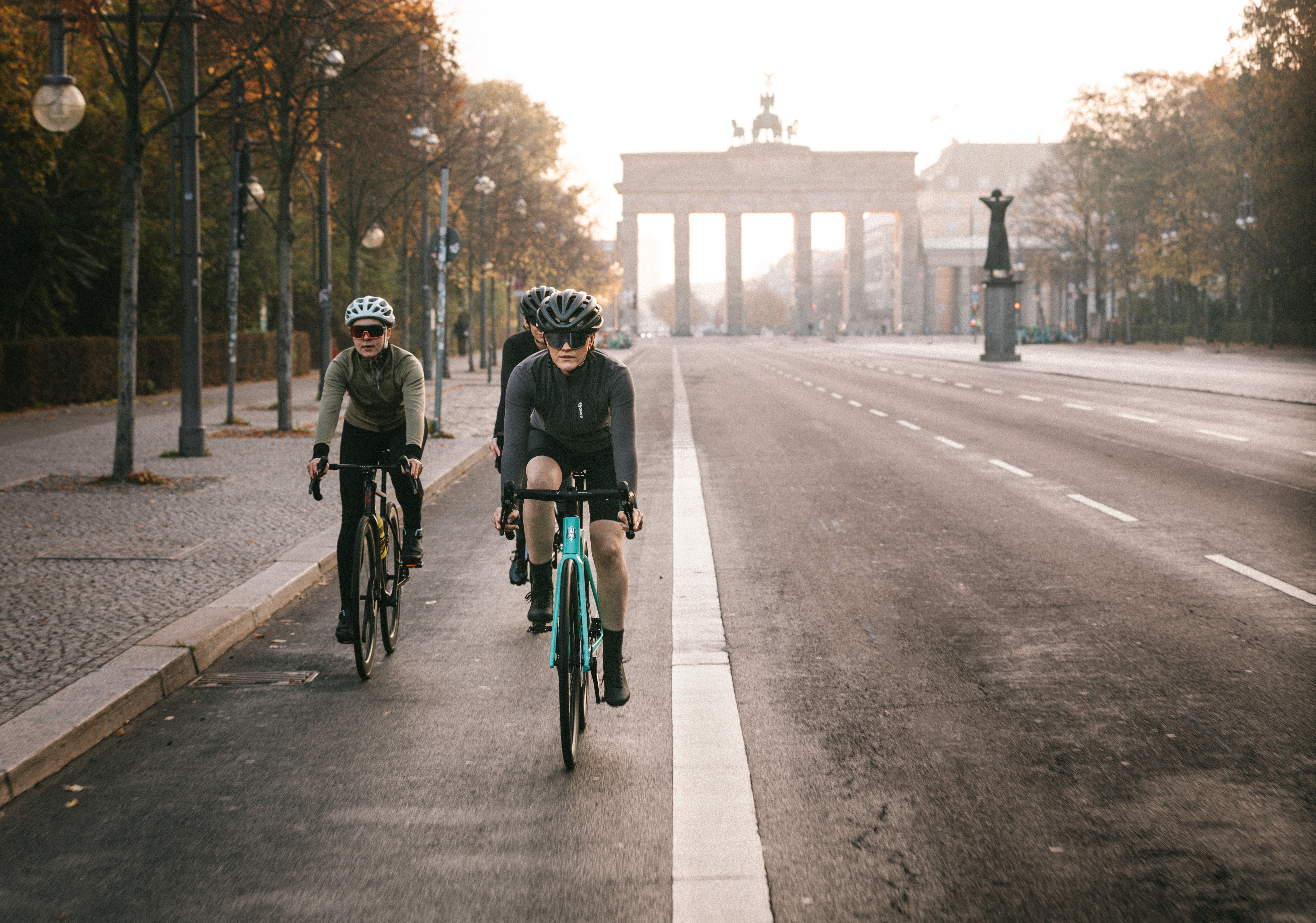 Drei Radfahrerinnen fahren am frühen Morgen auf leerer Straße in Richtung Brandenburger Tor.