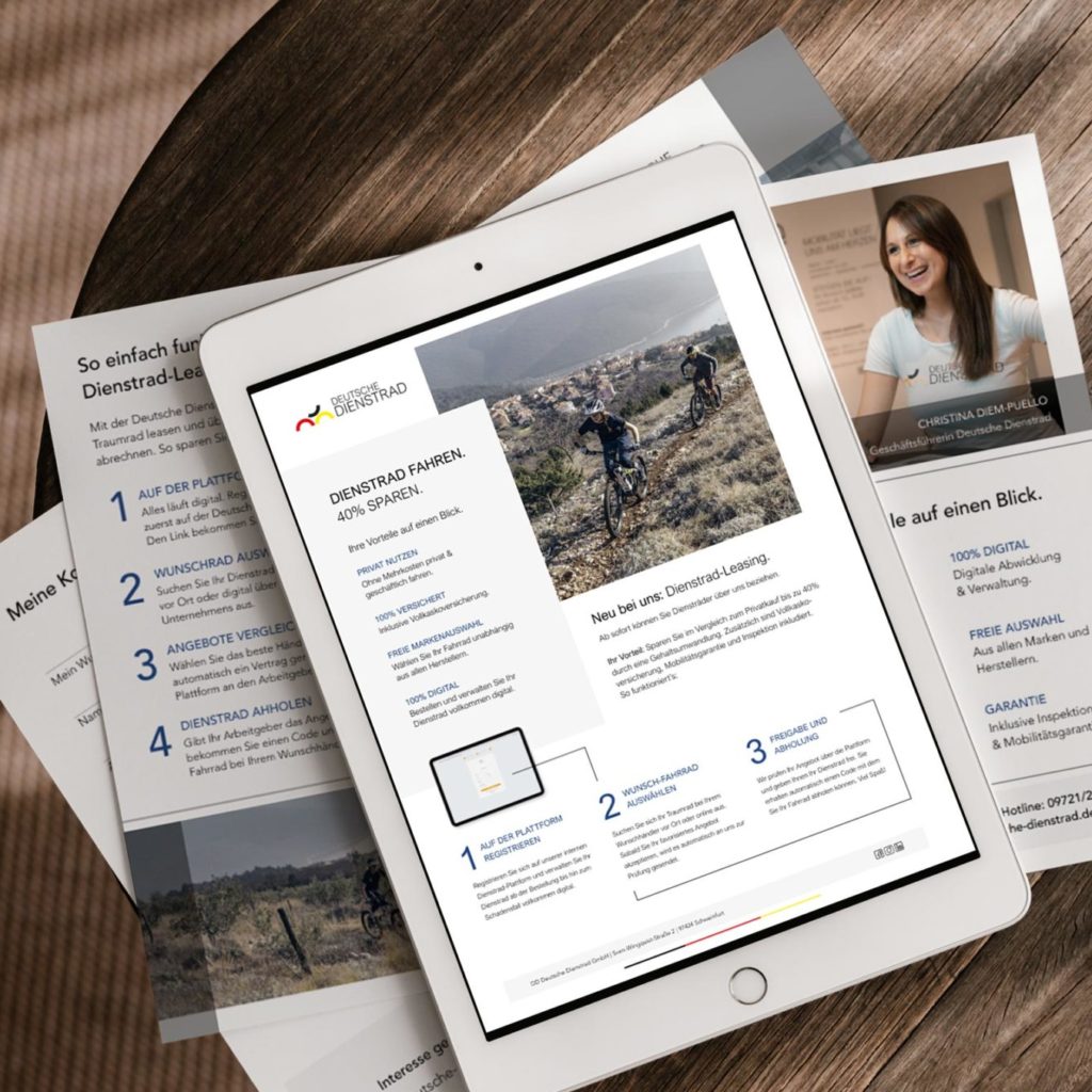 Ein Tablet liegt auf einem Tisch, auf dem Bildschirm wird eine Seite über "Dienstrad Leasing" angezeigt. Unter dem Tablet sind Broschüren ausgelegt, die ebenfalls Informationen über Dienstrad-Leasing enthalten. Auf einer der Broschüren ist das Foto einer Frau mit dem Namen "Christina Diem-Puello" zu sehen.