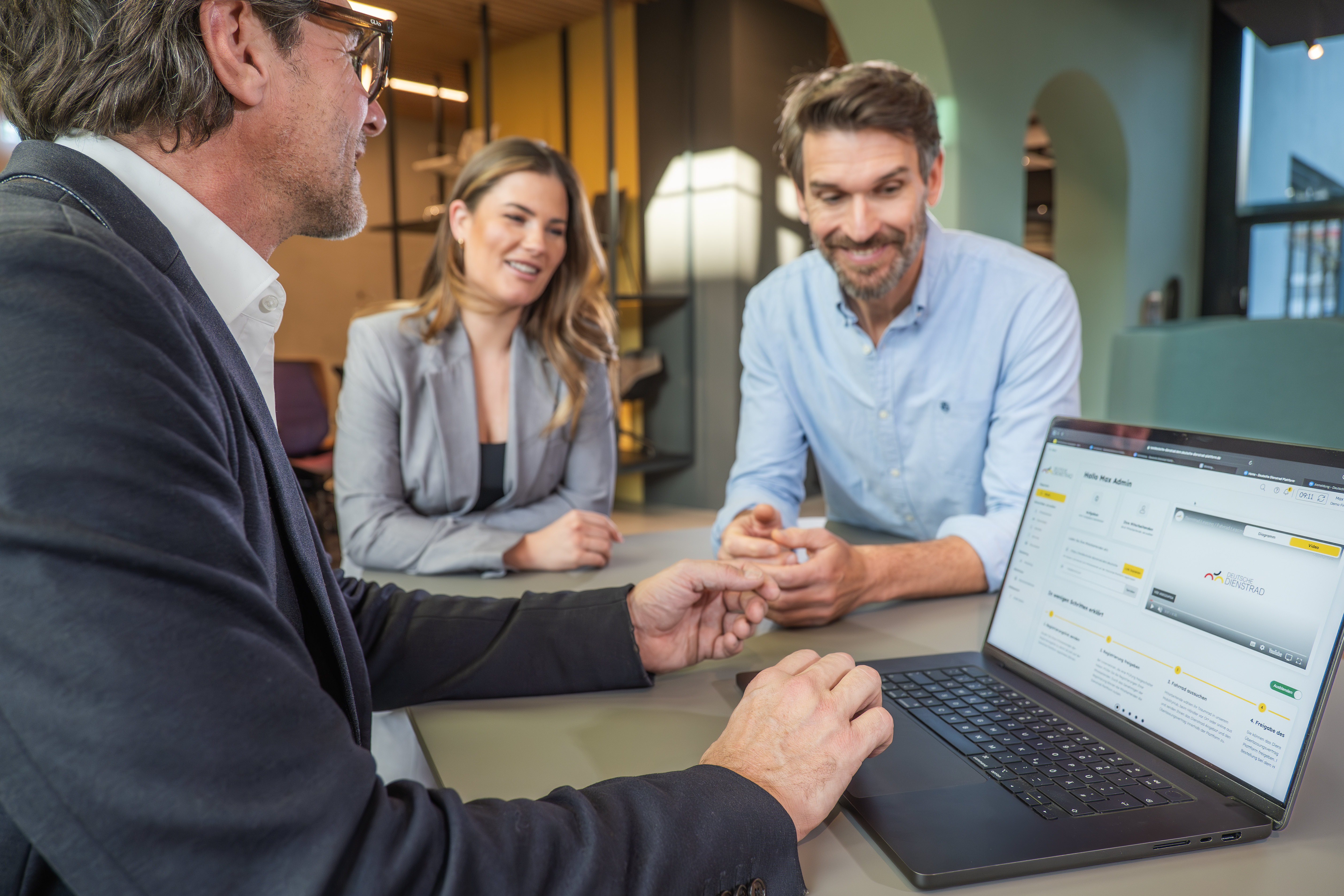 Drei Kolleg:innen stehen in einem modernen Büro zusammen und besprechen am Laptop eine Webseite auf dem Bildschirm.