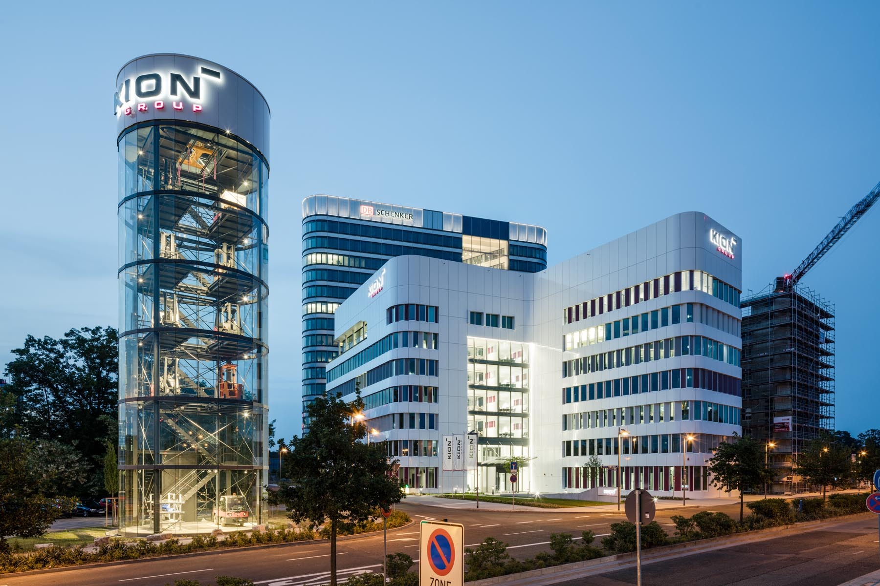 Moderne Bürogebäude bei Dämmerung, mit einem runden Glasturm auf der linken Seite und mehreren hohen Gebäuden im Hintergrund.